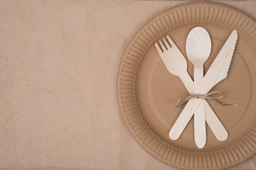 Top above overhead view photo of a set of wooden cutlery lying on a paper plate placed to the right side isolated on craft paper background table
