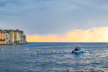 Fototapeta na wymiar Rovinj, Croatia; 7/18/2019: Boat sailing in the Adriatic Sea during sunset of a cloudy day with the typical croatian houses on the left