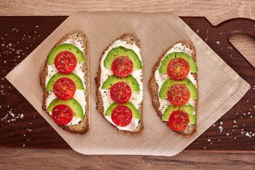 Healthy food, tomato and avocado toasts on a wooden cutting table, top view.