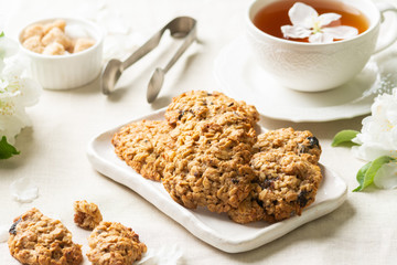Oatmeal cookies cookies in a white ceramic plate on a light table among flowering branches. Healthy homemade oatmeal cookies. A plate of cookies and a Cup of tea on the table
