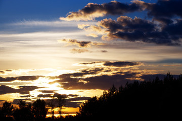 This is a sunset with clouds and woods.
