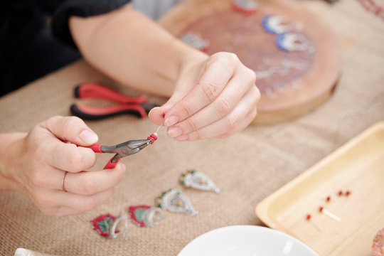 Close-up image of woman holding headpin with pilers and threading beads made of natural stones