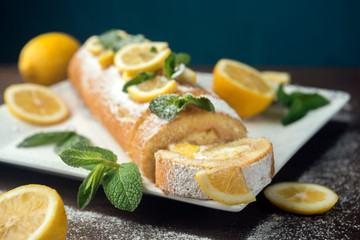 Lemon roll cake decorated with slices of lemon fruit and leaves of mint