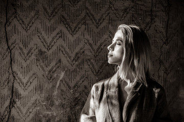 Sad woman with shadows on face in flat with aged wall