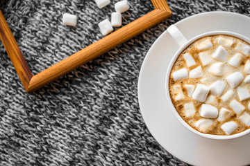 A white Cup of coffee with marshmallows on a gray background. Next to the Cup is a wooden photo frame and some marshmallows