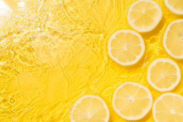 Slice of lemon underwater or in water with splashing and droplet top view flat lay on yellow background - obrazy, fototapety, plakaty