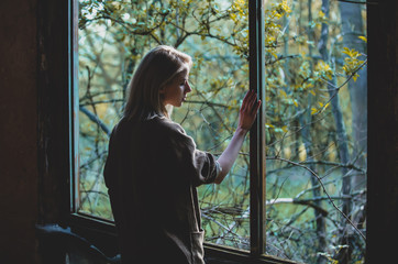 Woman stands with her back to the camera near window in a garden