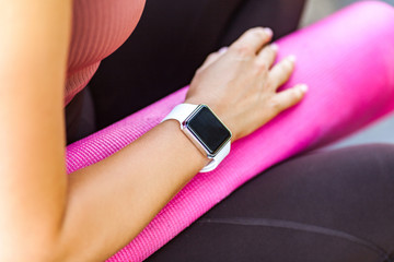 Closeup woman holding pink yoga mat, smartwatch on her hand with black empty display for time or pulse indicator after sport trainings, technology device with calories count app, weight loss program