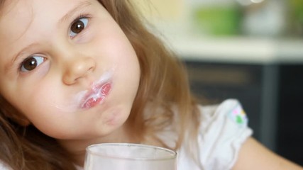 Child drinking milk drink - yogurt, smoothies. Baby girl holding a glass in her hands and drinks cocktail. Portrait close up.