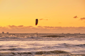 Extreme Sport Kitesurfing, cargo ships on the horizon. Surfer in the sea at Scheveningen at sunset