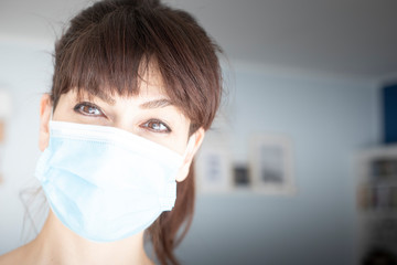 Caucasian attractive woman with ponytail and bangs, wearing surgical blue face mask during covid-19 or coronavirus pandemic. Copy space on the right.
