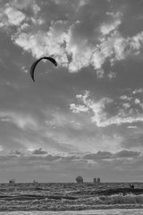 Extreme Sport Kitesurfing, cargo ships on the horizon. Surfer in the sea at Scheveningen at sunset. Black and white