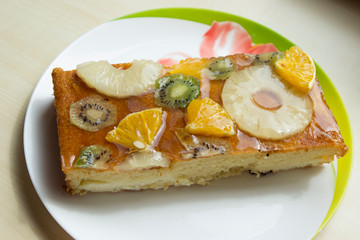 A large piece of cheesecake diet cake pie with canned fruits (pineapple, orange, kiwi) and with jelly on top.