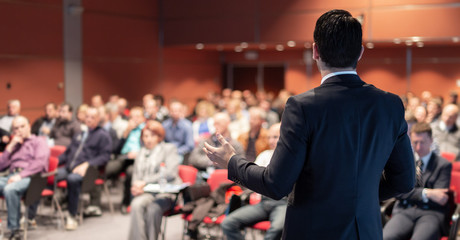 Speaker giving a talk on corporate business conference. Unrecognizable people in audience at...