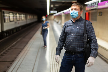 Man in protective medical mask is standing on platform and waiting train in the underground.