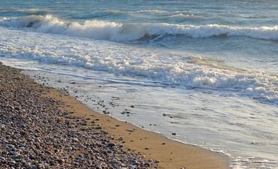 sea ​​waves at the sandy-stone coast with sunset. rocks in the sea and strong waves