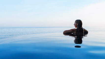 Happy girl enjoy on summer beach holiday. Young woman relaxing at edge of infinity swimming pool...