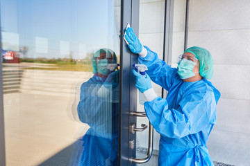 Reinigungskraft bei Desinfektion von Tür einer Klinik wegen Covid-19
