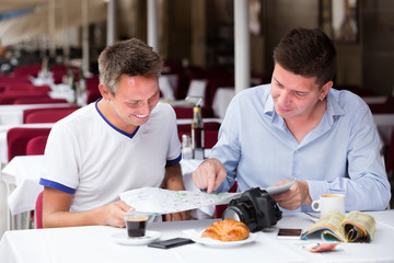 two happy men sitting with coffee and looking at map in cafe