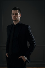 Fototapeta premium Young handsome businessman in black shirt and black suit. Confident young businessman posing on gray background