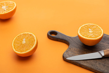 fresh juicy cut oranges on cutting board with knife on colorful background