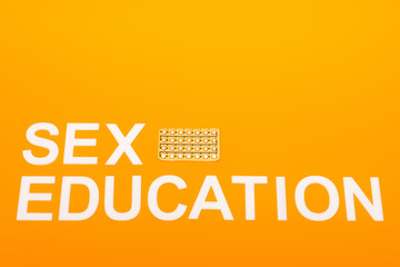 top view of sex education lettering near blister pack with contraceptive pills isolated on orange