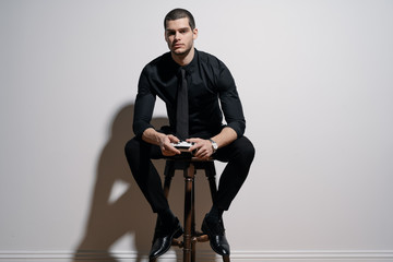 Young handsome businessman in black shirt and black suit. Confident young businessman posing on white background. Holding a game joystick © arthurhidden