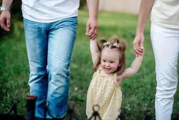 Dad and mom lead their funny one-year-old daughter in the park in summer

