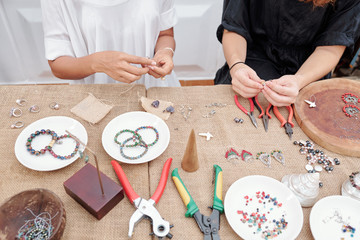 Women using various tools when making beautiful jewelry like earrings and bracelets with natural...