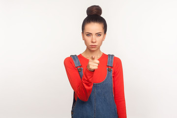 Hey you! Portrait of bossy dissatisfied angry girl with hair bun in denim overalls pointing finger...