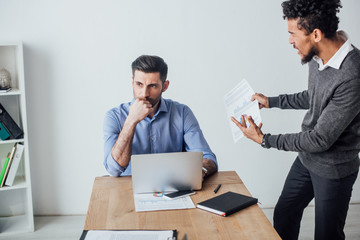 Angry african american businessman quarreling at colleague near laptop in office