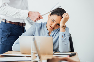 Selective focus of businessman holding document near head of sad mexican colleague in office