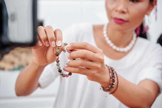 Woman filming how to use clasp of bracelet she made at home with beautiful natural stones