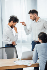 Selective focus of businessman pointing at offended african american colleague in office