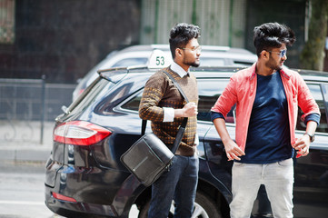 Two young stylish indian man frieds model posing in street against black taxi car.