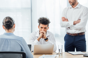 Selective focus of thoughtful african american businessman sitting near colleagues in office