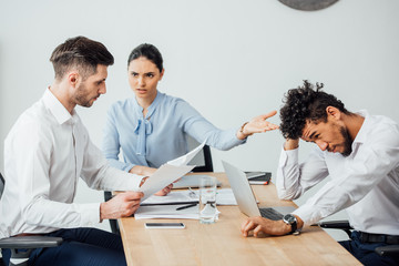 Angry mexican businesswoman pointing at african american colleague to colleague with papers in office
