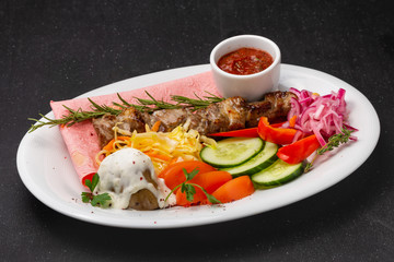 Meat skewers on a plate with vegetables, traditional meat food on fire