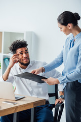 Selective focus of african american man looking at mexican businesswoman with clipboard in office