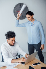 Selective focus of scared african american businessman using laptop near angry mexican businesswoman