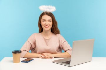 Lovely angelic happy woman employee with nimbus sitting at workplace and looking at camera with...