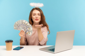 Beautiful angelic woman with nimbus sitting at laptop, holding dollar banknotes and sending sensual...