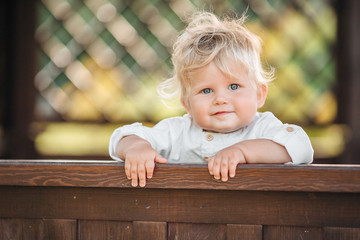 A pretty boy 1 year old smiling with long blond hair on a Sunny summer