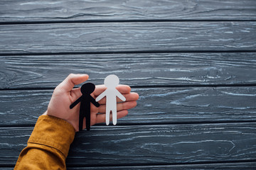 High angle view of man holding white and black human figures on dark wooden surface