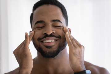 Close up of happy african American metrosexual young man massage face do beauty morning procedures...