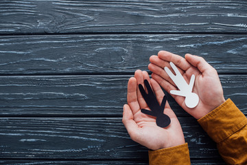 Top view of paper black and white human figures in male hands on dark wooden background