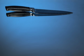 A large knife sits on a mirror background