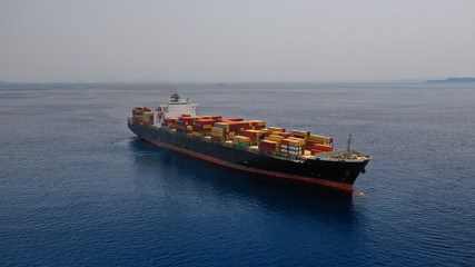Aerial drone photo of huge container cargo Ship carrying load in truck-size colourful containers cruising deep blue open ocean Mediterranean sea 