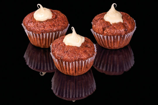 Tasty chocolate muffins with cream, isolated on black background, with reflection