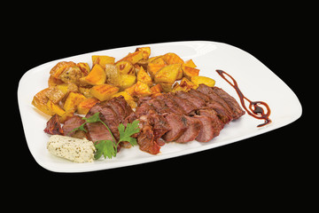 Gourmet beef steak served with boiled potatoes in a plate, isolated on black background.